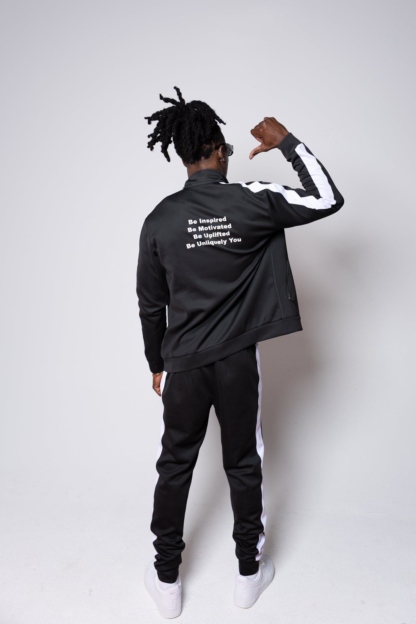 Men’s black slim-fit performance tracksuit with white side stripe detailing, featuring a zip-up jacket and tapered joggers, styled with white sneakers for a clean, athletic streetwear look built for comfort, confidence, and everyday performanc