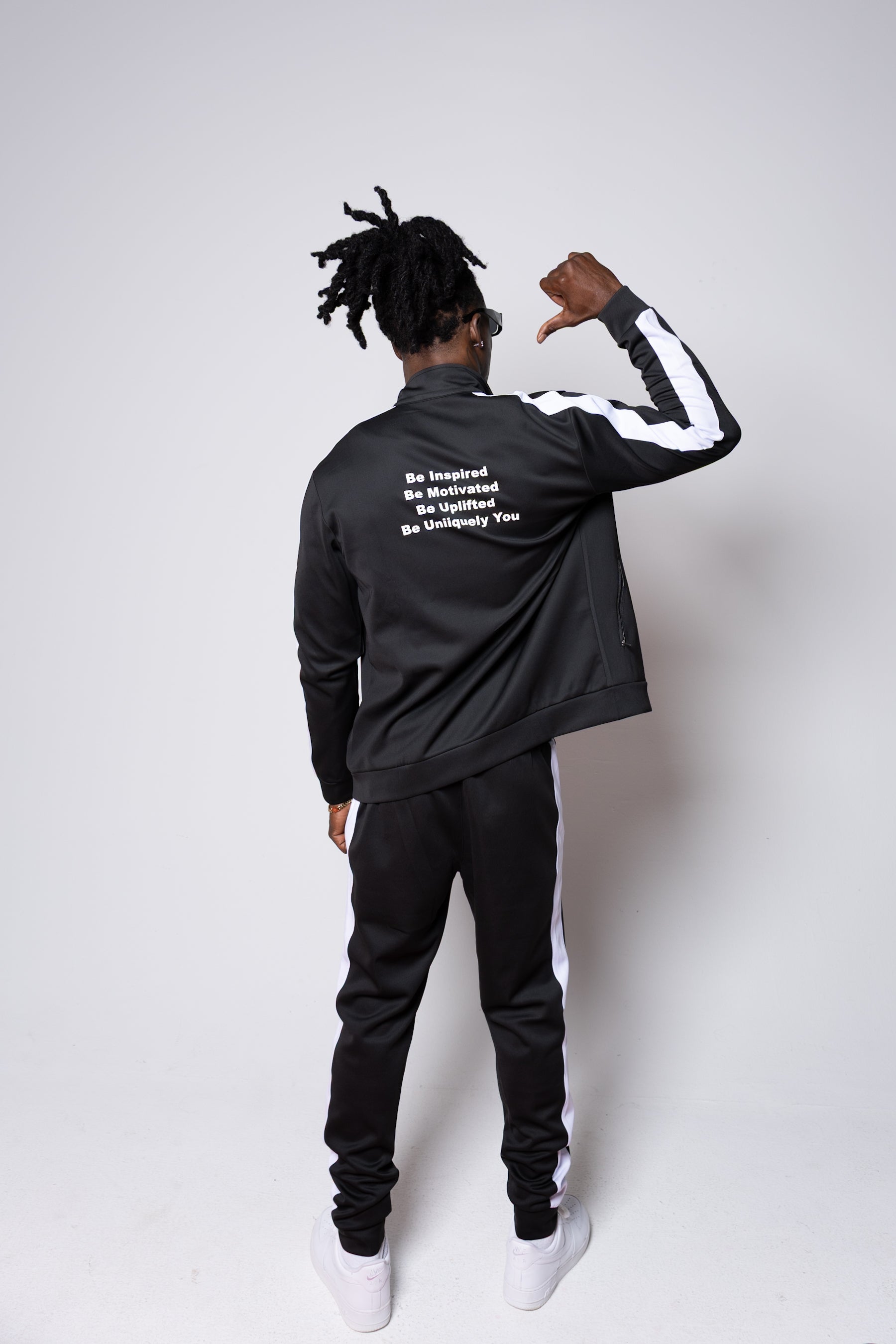 Men’s black slim-fit performance tracksuit with white side stripe detailing, featuring a zip-up jacket and tapered joggers, styled with white sneakers for a clean, athletic streetwear look built for comfort, confidence, and everyday performanc