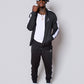 Men’s black slim-fit performance tracksuit with white side stripe detailing, featuring a zip-up jacket and tapered joggers, styled with white sneakers for a clean, athletic streetwear look built for comfort, confidence, and everyday performance.