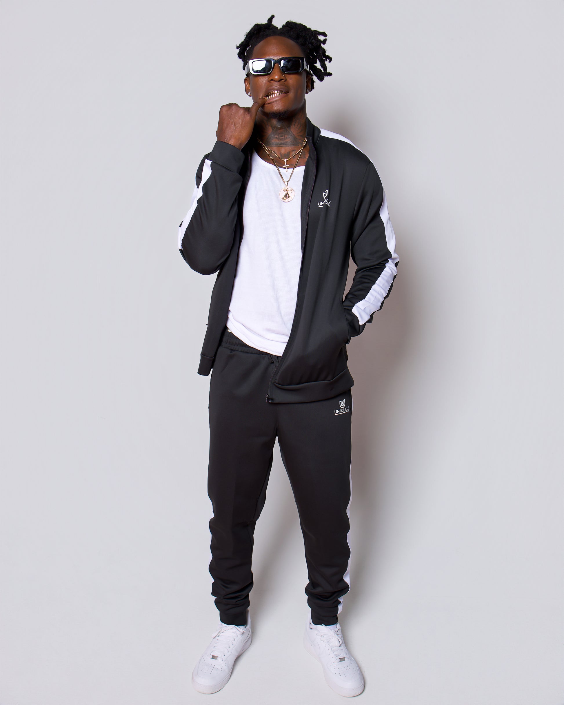 Men’s black slim-fit performance tracksuit with white side stripe detailing, featuring a zip-up jacket and tapered joggers, styled with white sneakers for a clean, athletic streetwear look built for comfort, confidence, and everyday performance.
