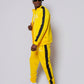 Men’s bold yellow slim-fit tracksuit with black side stripes, featuring a sleek zip-up jacket and tapered joggers, styled with white sneakers for a clean, modern athleisure look built for confidence, comfort, and standout style.