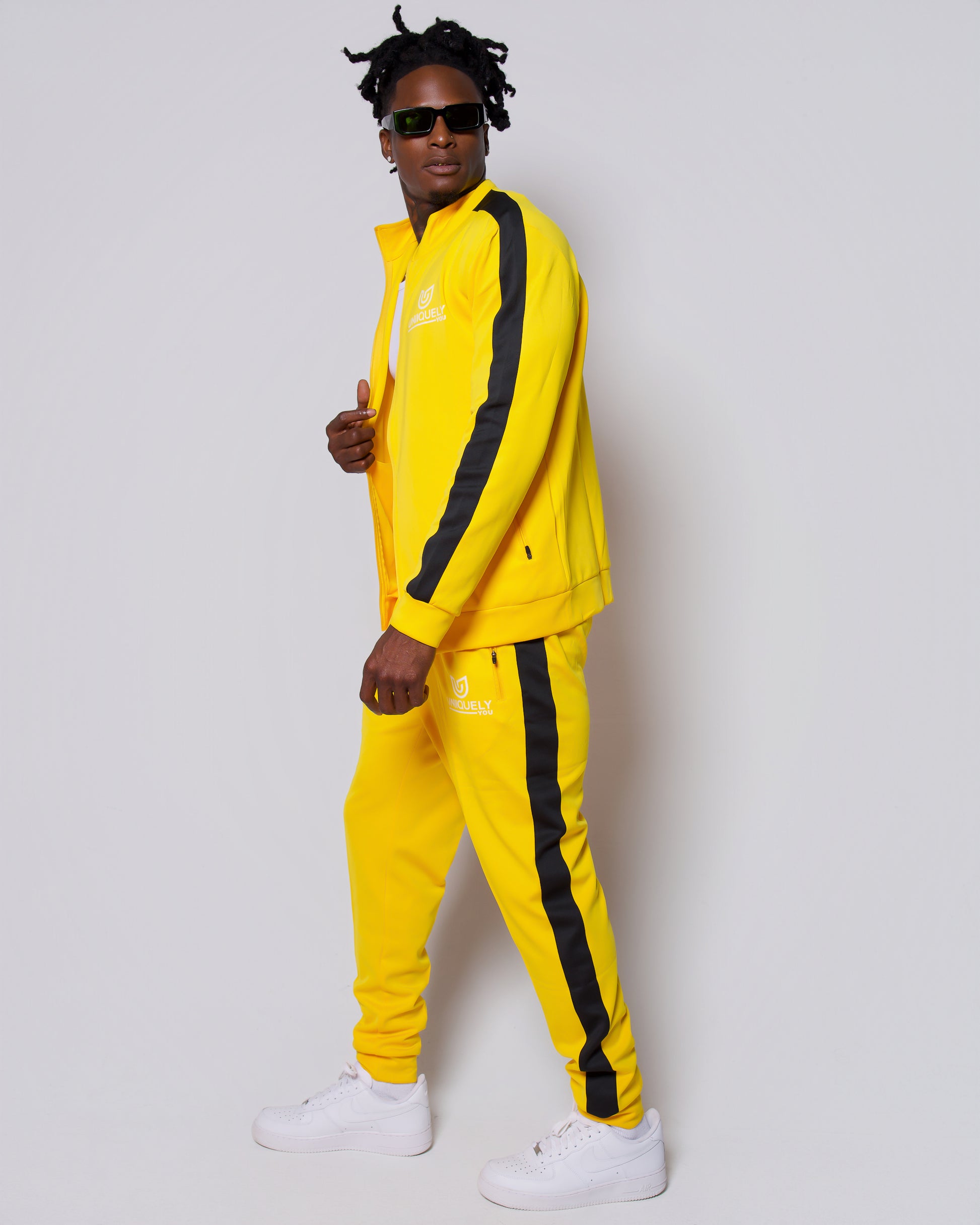 Men’s bold yellow slim-fit tracksuit with black side stripes, featuring a sleek zip-up jacket and tapered joggers, styled with white sneakers for a clean, modern athleisure look built for confidence, comfort, and standout style.