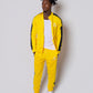 Men’s bold yellow slim-fit tracksuit with black side stripes, featuring a sleek zip-up jacket and tapered joggers, styled with white sneakers for a clean, modern athleisure look built for confidence, comfort, and standout style.