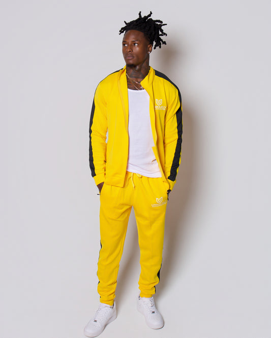 Men’s bold yellow slim-fit tracksuit with black side stripes, featuring a sleek zip-up jacket and tapered joggers, styled with white sneakers for a clean, modern athleisure look built for confidence, comfort, and standout style.