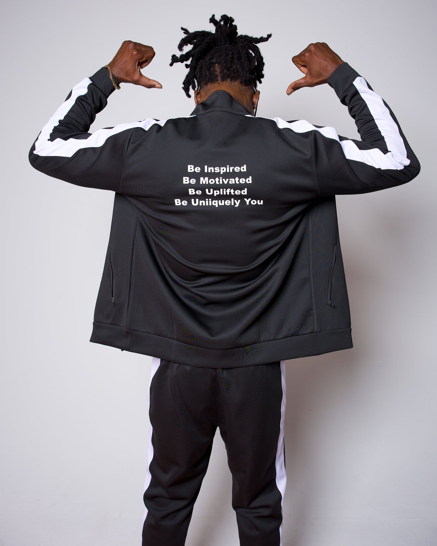 Men’s black slim-fit performance tracksuit with white side stripe detailing, featuring a zip-up jacket and tapered joggers, styled with white sneakers for a clean, athletic streetwear look built for comfort, confidence, and everyday performance.