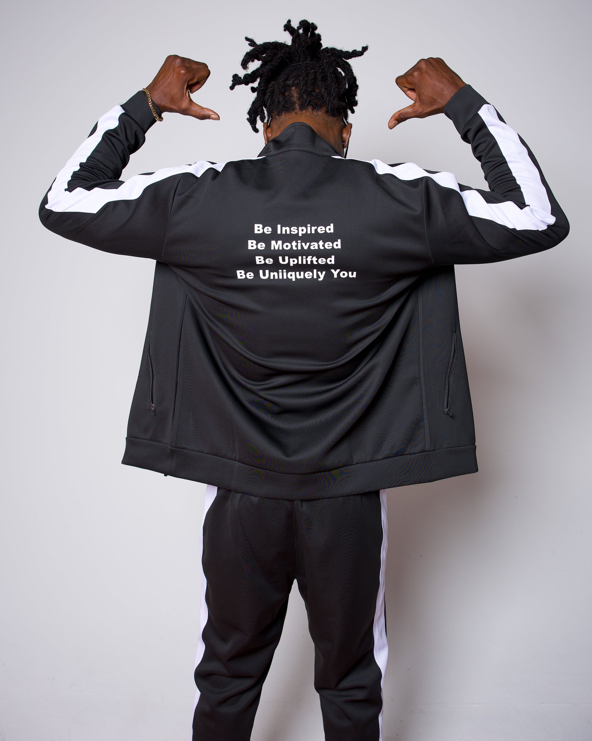 Men’s black slim-fit performance tracksuit with white side stripe detailing, featuring a zip-up jacket and tapered joggers, styled with white sneakers for a clean, athletic streetwear look built for comfort, confidence, and everyday performance.
